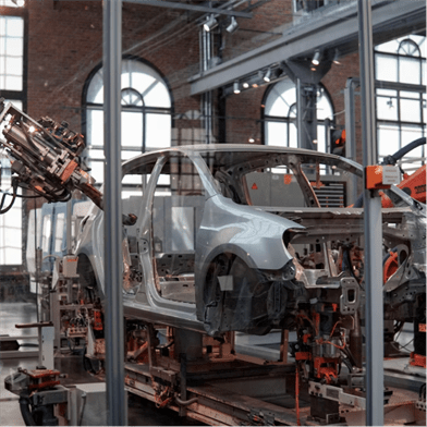 A partially assembled car chassis is positioned on an automated assembly line within a spacious, well-lit industrial facility.