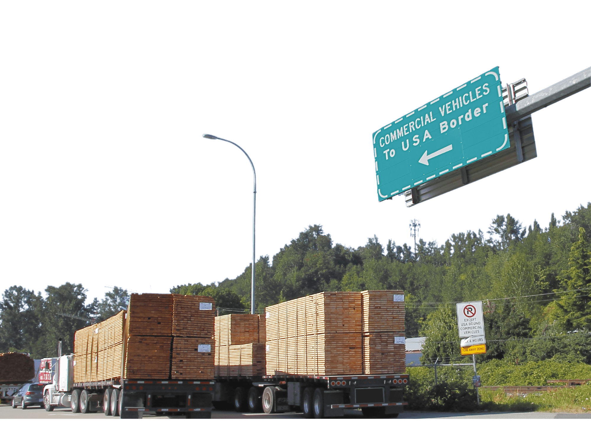 A highway with large semi-trailer trucks carrying lumber and a sign overhead reading 