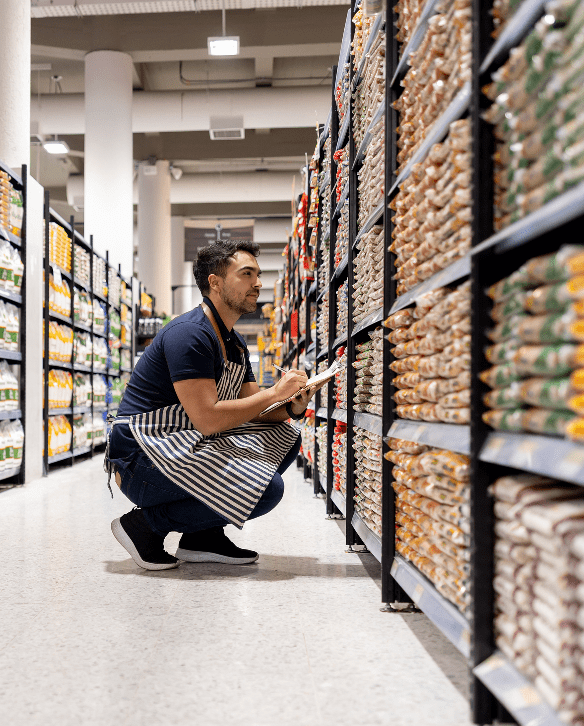 Store employee checking inventory on fully stocked food shelves in a grocery aisle.