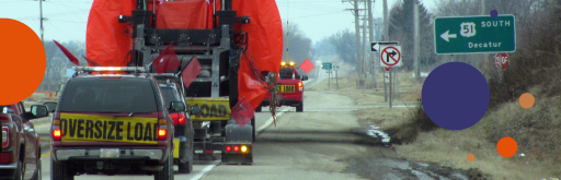 Convoy of escort vehicles transporting an oversized load on a rural road.