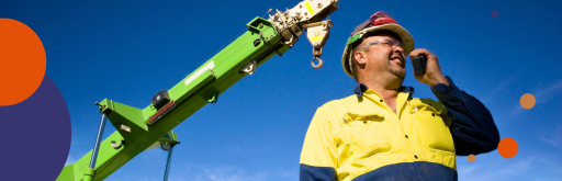 Rigger in safety gear using a radio next to a crane.