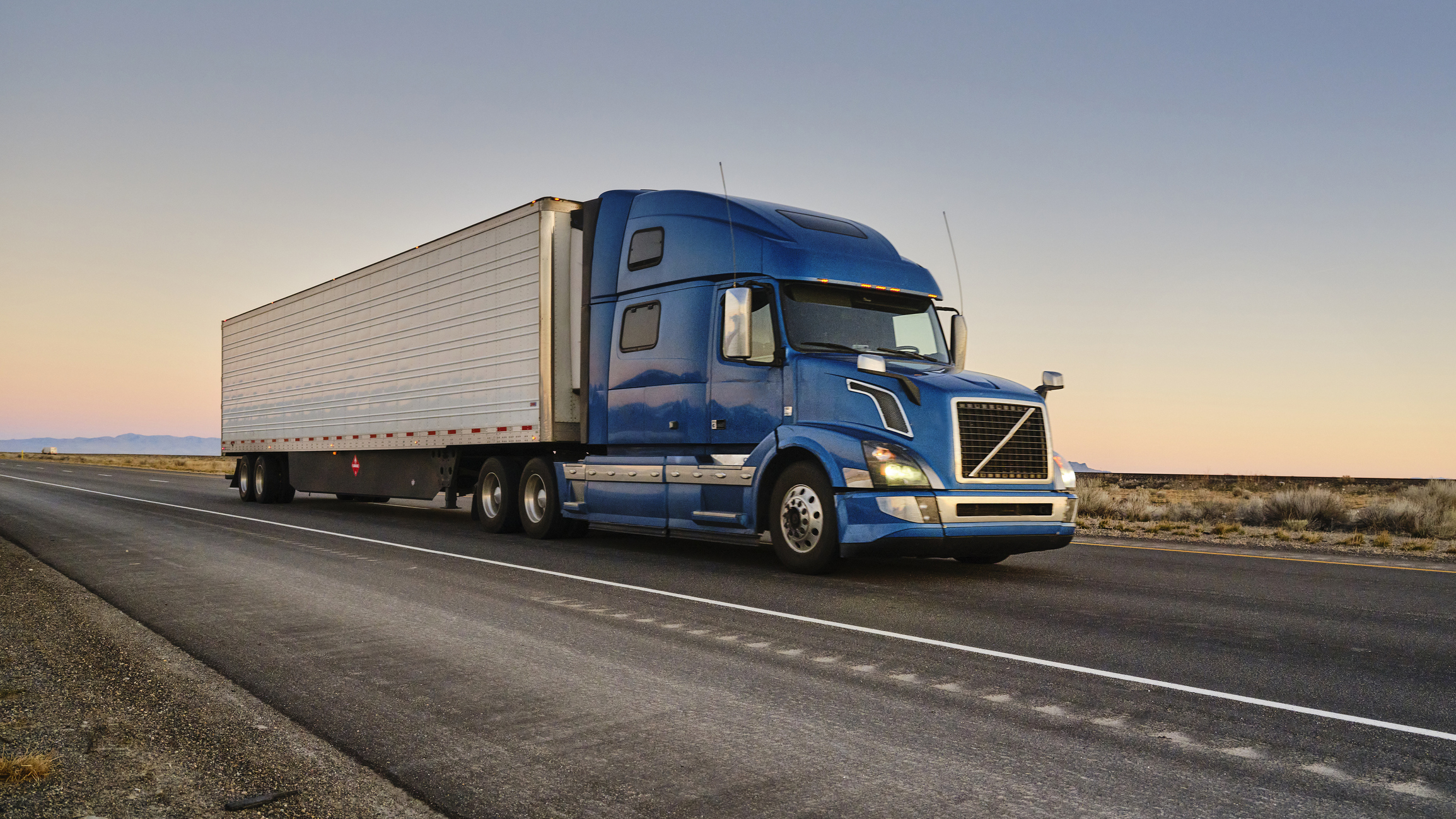 Blue freight truck driving across North America at sunset, symbolizing efficient cross-border logistics and bonded transport.